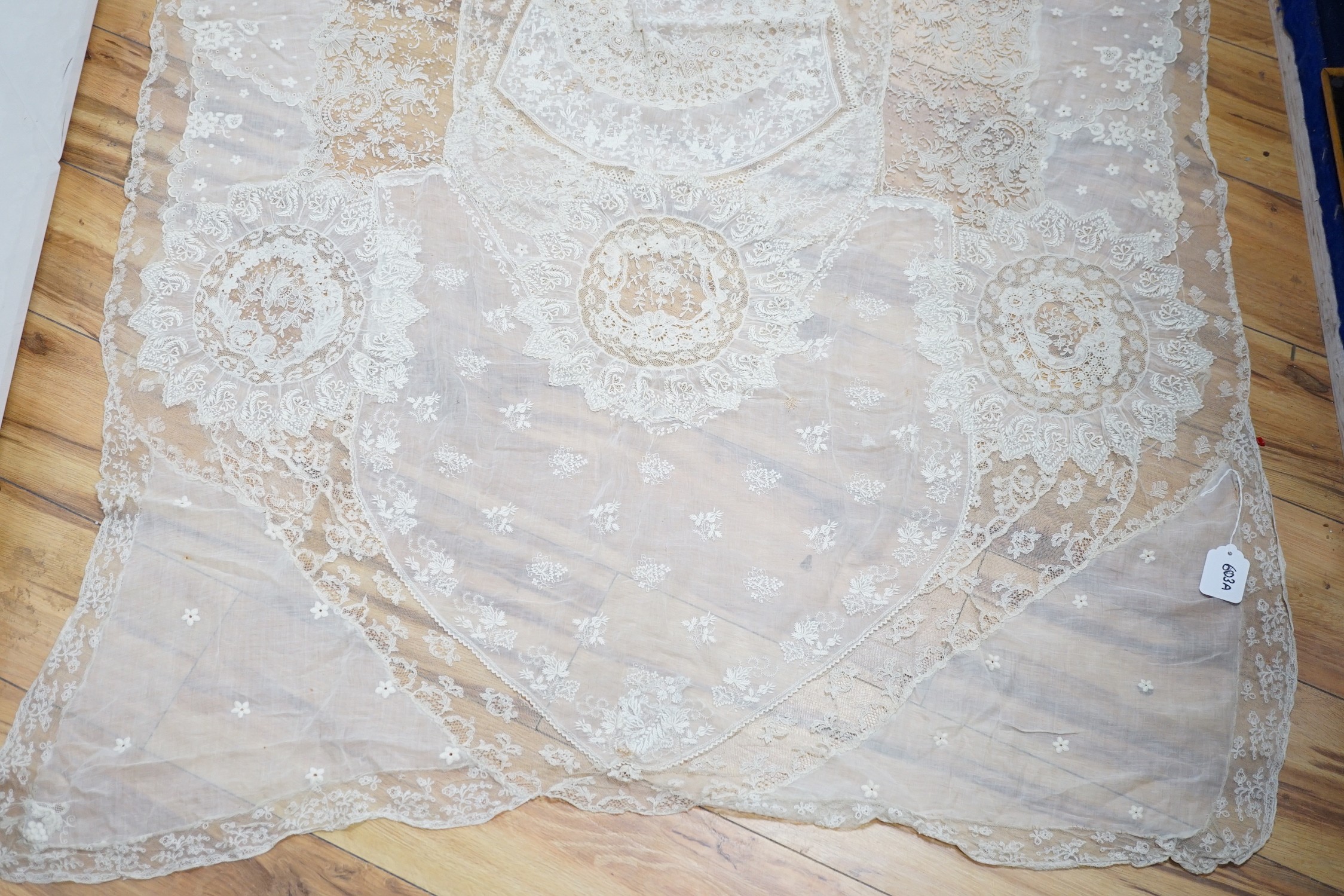 A late 19th century Normandy lace table cover of hand spun linen, hand white worked, with Brussels Point de Gaze insertions and bobbin lace edging, together with two feathers and a net veil